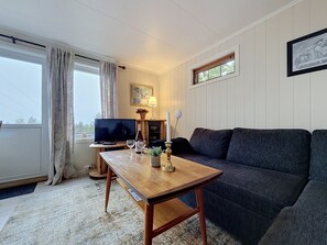 Et møbleret opholdsstue med et træbord, en mørk sofa, et fjernsyn og et vindue med gardiner.