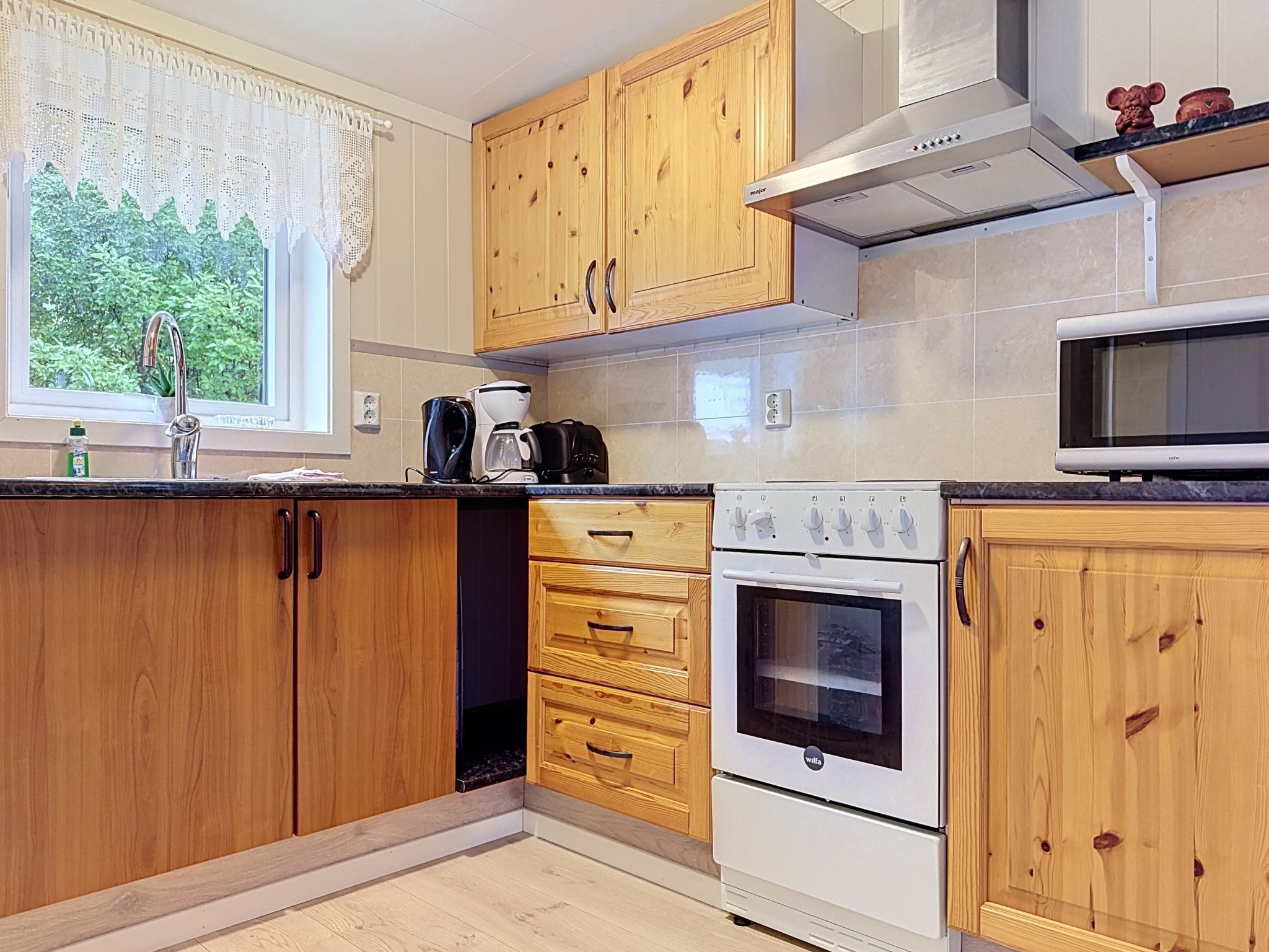 A kitchen with wooden cabinets, a built-in oven, a microwave, and a window with a view of greenery.