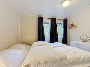 A bedroom with a bed, a window with curtains, a bedside table with a lamp, and a wall-mounted hanger. - Lihesten by Interhome (Sørbøvåg)
