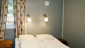 A bedroom with two beds, a wooden nightstand, a window with curtains, and two wall-mounted lamps. - Fjordperlen by Interhome (Sørbøvåg)