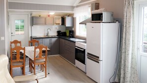 A compact kitchen with a refrigerator, microwave, and stove. There is a dining area with a table and chairs. - Fjordperlen by Interhome (Sørbøvåg)