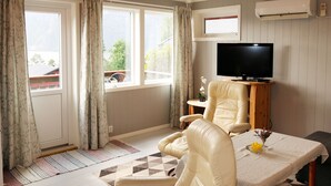A living room with a sofa, a TV, and a table with a vase. - Fjordperlen by Interhome (Sørbøvåg)