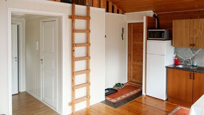 A compact kitchen with wooden cabinets, a microwave, and a refrigerator. A wooden ladder is leaning against the wall, and a red rug is on the floor. - Vacation home Oasen by Interhome (Sørbøvåg)