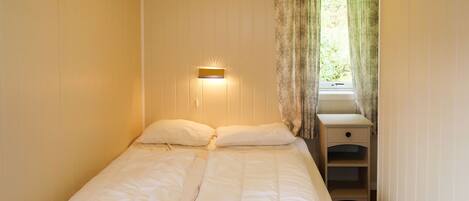 A neatly made bed with white bedding in a room with wooden walls and a small bedside table with drawers.