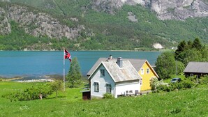 Une maison avec un drapeau, un lac et des montagnes en arrière-plan.