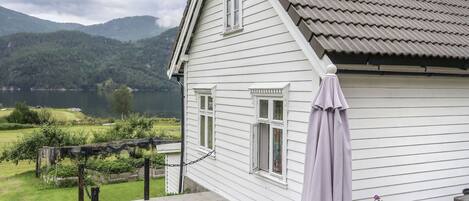 A white house with a deck, a pergola, and a view of a lake and mountains.