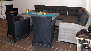 A furnished outdoor area with a sofa, chairs, a table, and a TV mounted on the wall.
