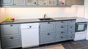 A modern kitchen with grey cabinets, a black countertop, a dishwasher, and an oven.