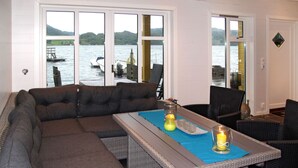 A modern living room with a sectional sofa, a dining table, and a view of a lake with boats.
