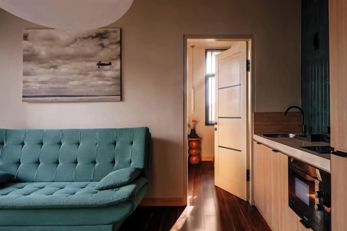 A compact living space with a sofa, a painting, a kitchen area with a stove, and a door leading to another room.