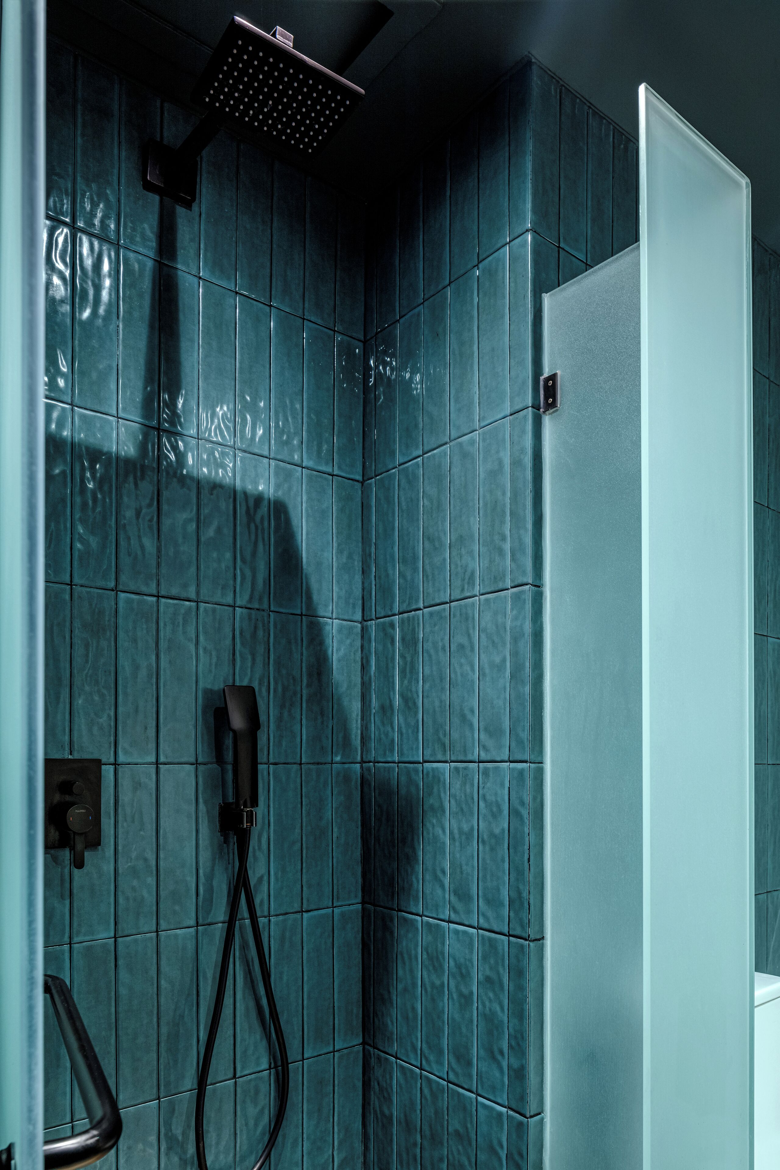 Une salle de bain avec des carreaux de couleur turquoise, une pomme de douche et des toilettes.