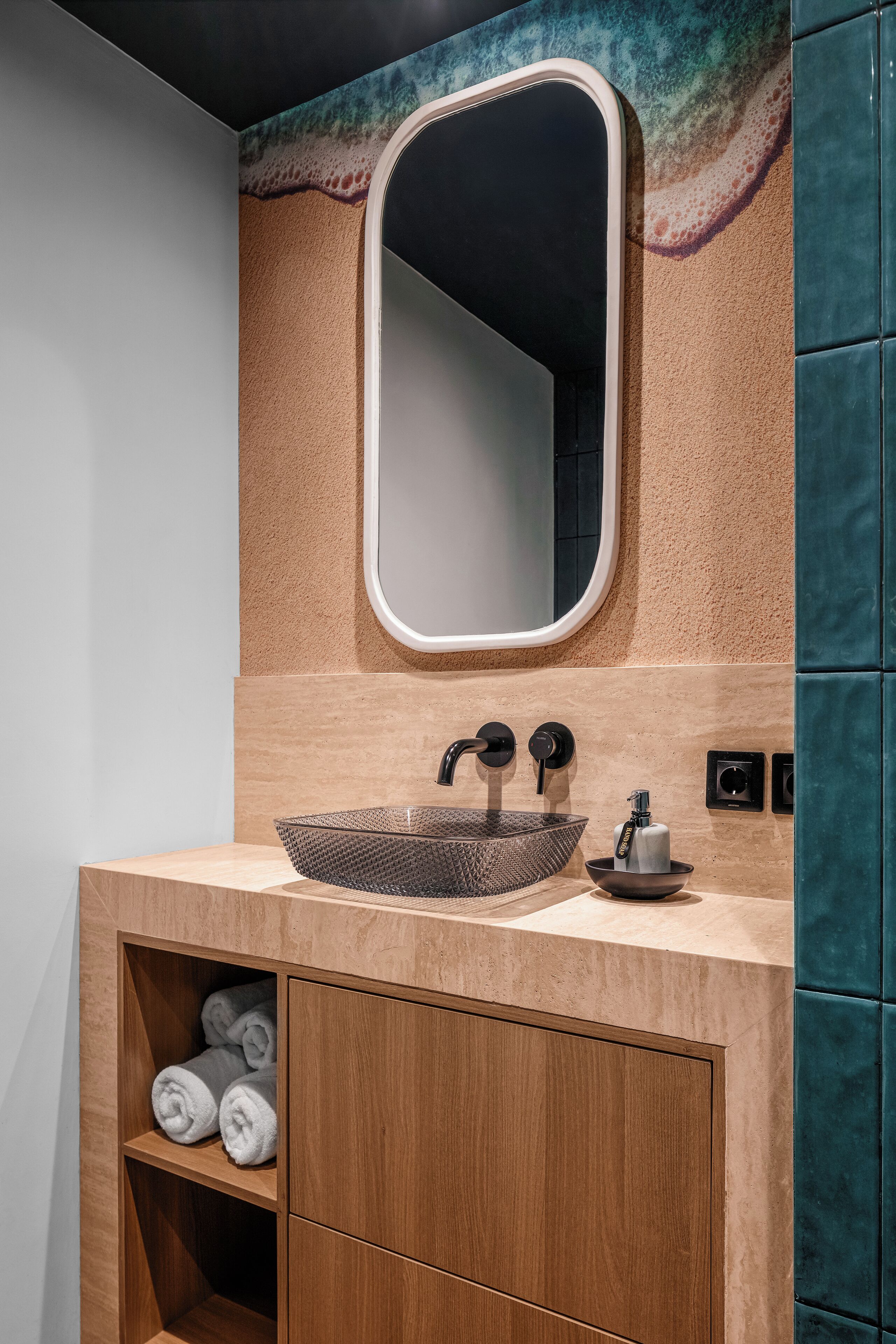 Un baño con un espejo ovalado grande, un lavamanos texturizado y un armario de madera con toallas.