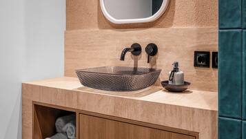 Un baño con un espejo ovalado grande, un lavamanos texturizado y un armario de madera con toallas.