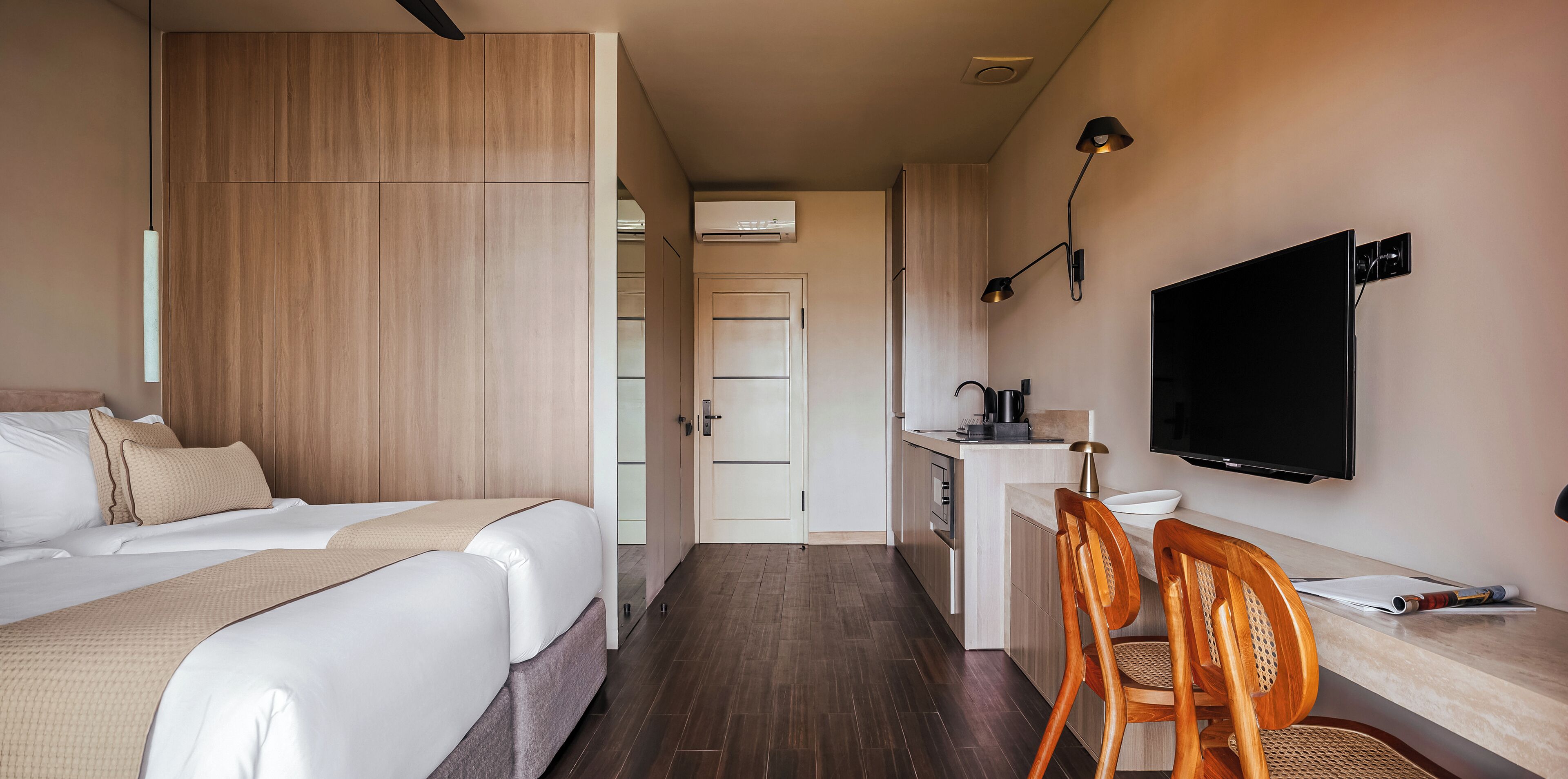 Ein Hotelzimmer mit zwei Betten, einem Schreibtisch mit Stuhl, einem Fernseher und einer Küchenzeile.