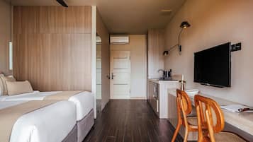 Ein Hotelzimmer mit zwei Betten, einem Schreibtisch mit Stuhl, einem Fernseher und einer Küchenzeile.