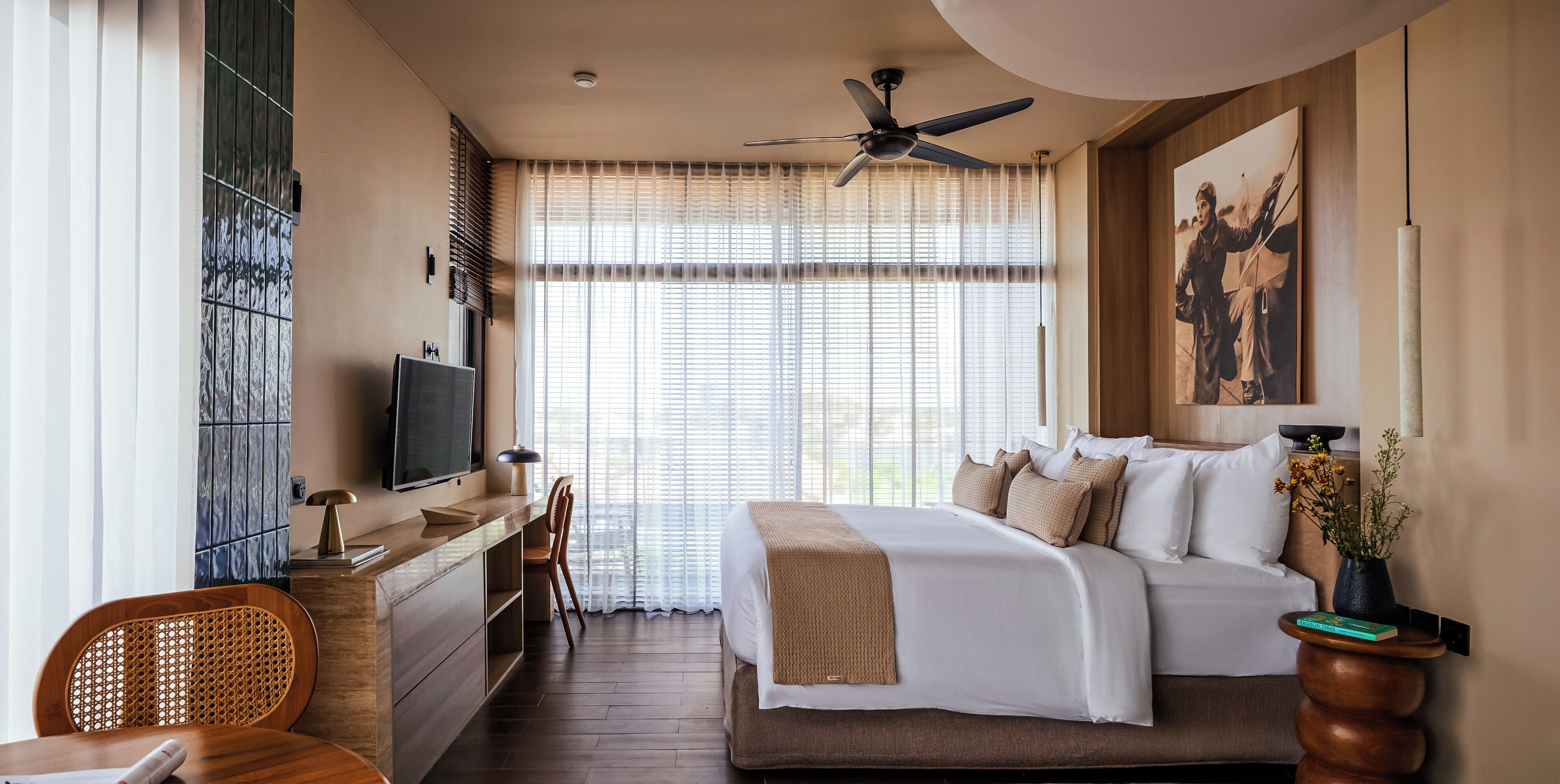 A hotel room with a bed, a desk, a chair, a television, and a ceiling fan.