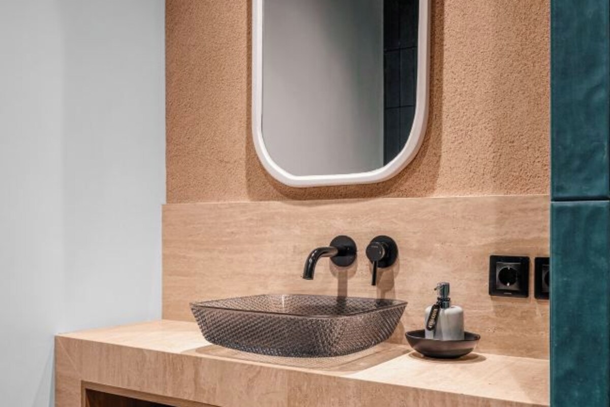 A modern bathroom with a glass bowl sink, two black faucets, and a small bowl on the countertop.