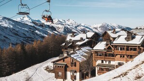 A ski resort with wooden buildings, ski lifts, and snow-covered mountains.