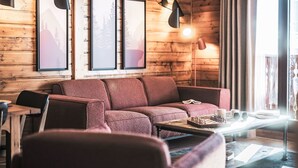 A cozy living room with a wooden wall, a red sofa, a coffee table with chess pieces, and framed pictures on the wall.