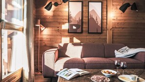 A cozy room with a wooden floor, a sofa, a coffee table with food and drinks, and framed pictures on the wall.