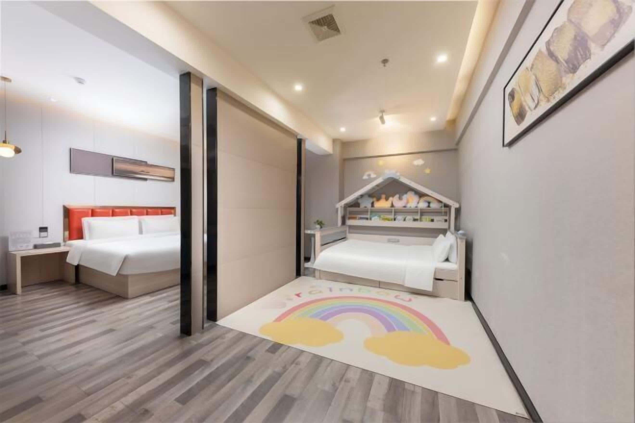A modern bedroom with a bed, bedside table, and a small play area with a rainbow rug.