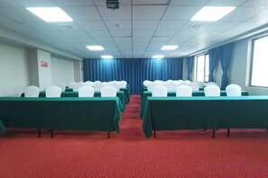 A conference room with rows of tables and chairs, a red carpeted floor, and a view through a window with blue curtains. - Star Sky Hotel (Pingjiang)