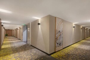 Pasillo de hotel con piso alfombrado, puertas a ambos lados y un gran mural en la pared.