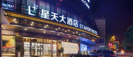A hotel with a large sign, a covered entrance, and a parking area.