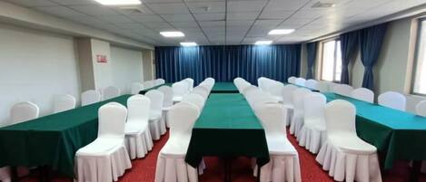 Uma sala de conferências com uma mesa comprida, cadeiras brancas e carpete vermelho.