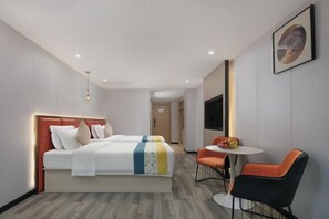 A hotel room with a large bed, a small table with chairs, and a TV on the wall.
