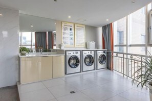 A laundry room with a washing machine, a dryer, and a sink. There is a bulletin board with information and a potted plant. - Star Sky Hotel (Pingjiang)