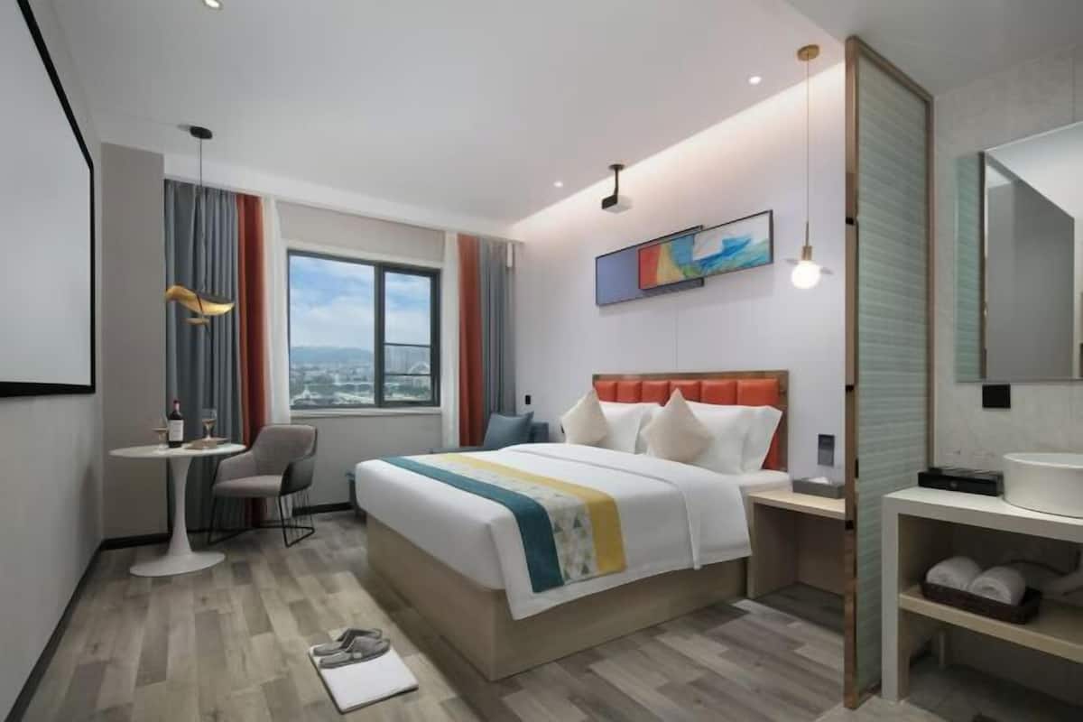 A modern hotel room with a large bed, a desk, a chair, and a view of the city.