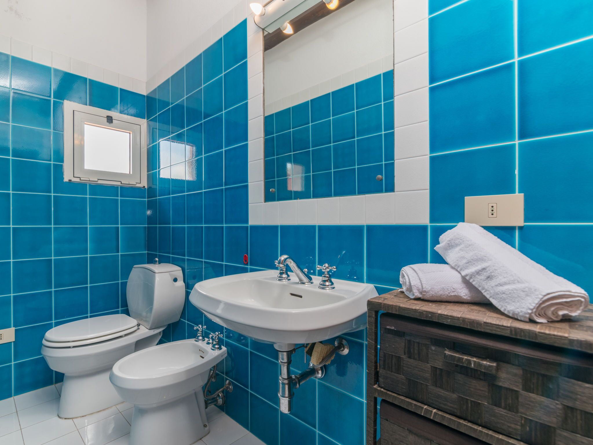 A bathroom with blue tiles, a white sink, a toilet, and a bidet.