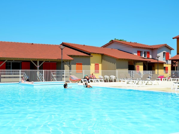 A swimming pool with lounge chairs and a building with red roofs and white railings.