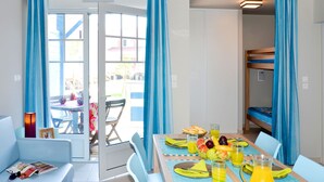 Une pièce lumineuse avec une table à manger dressée pour deux personnes, un lit superposé et un canapé.