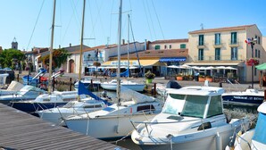 Un port de plaisance où sont amarrés plusieurs bateaux, un bâtiment abritant un restaurant appelé « La Luna », et une rue bordée de boutiques et de cafés.