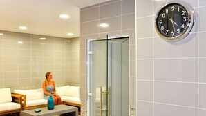 Une salle de spa moderne dotée d’une douche à parois de verre, d’un coin salon avec un banc et d’une horloge murale.