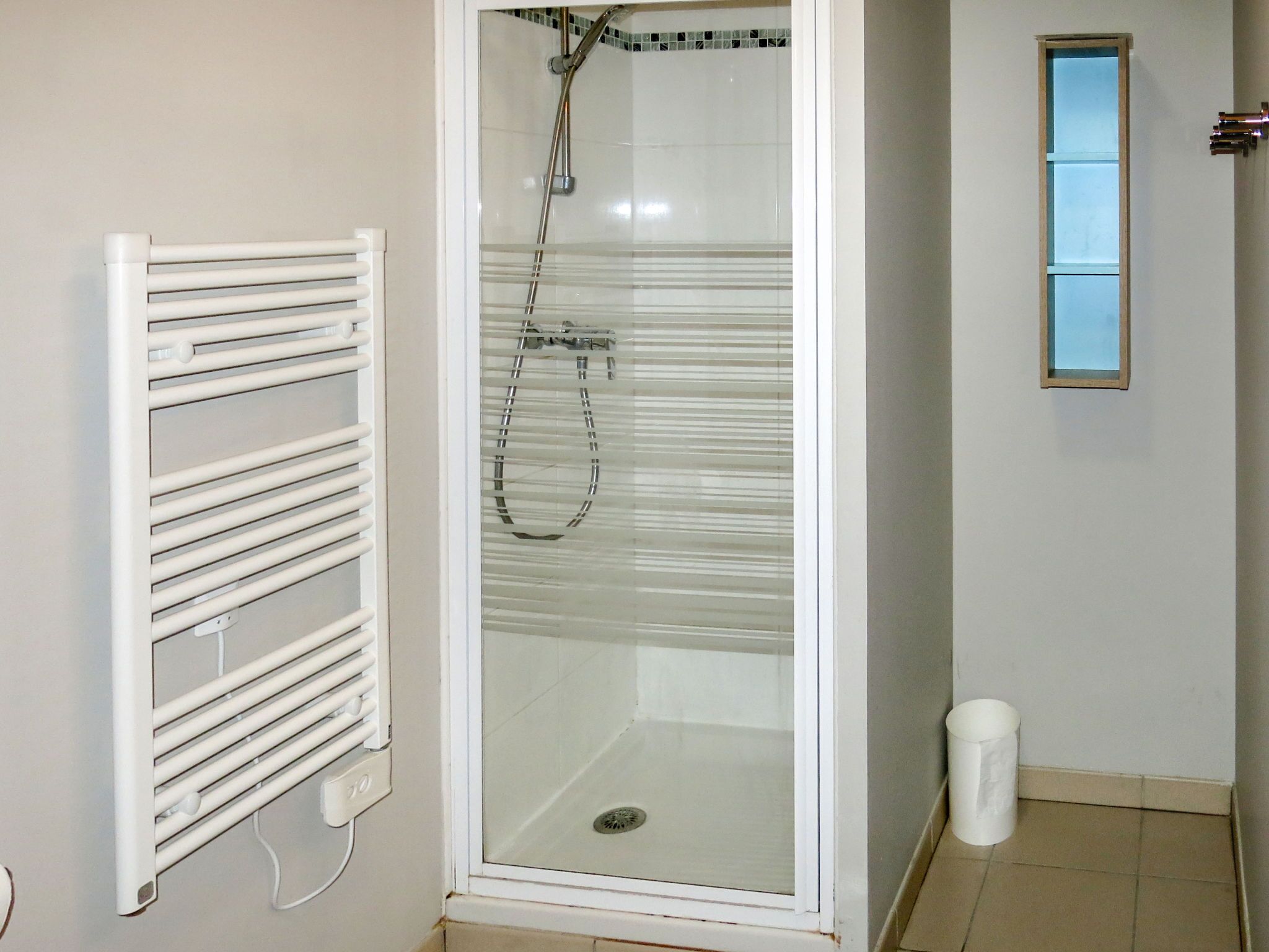 A bathroom with a glass-enclosed shower, a white radiator, and a small window.