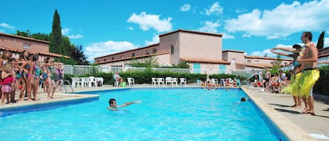 A swimming pool with people around it, a building with a tiled roof, and a clear blue sky.