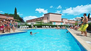 Una piscina rodeada de gente, un edificio con techo de tejas y un cielo azul despejado.