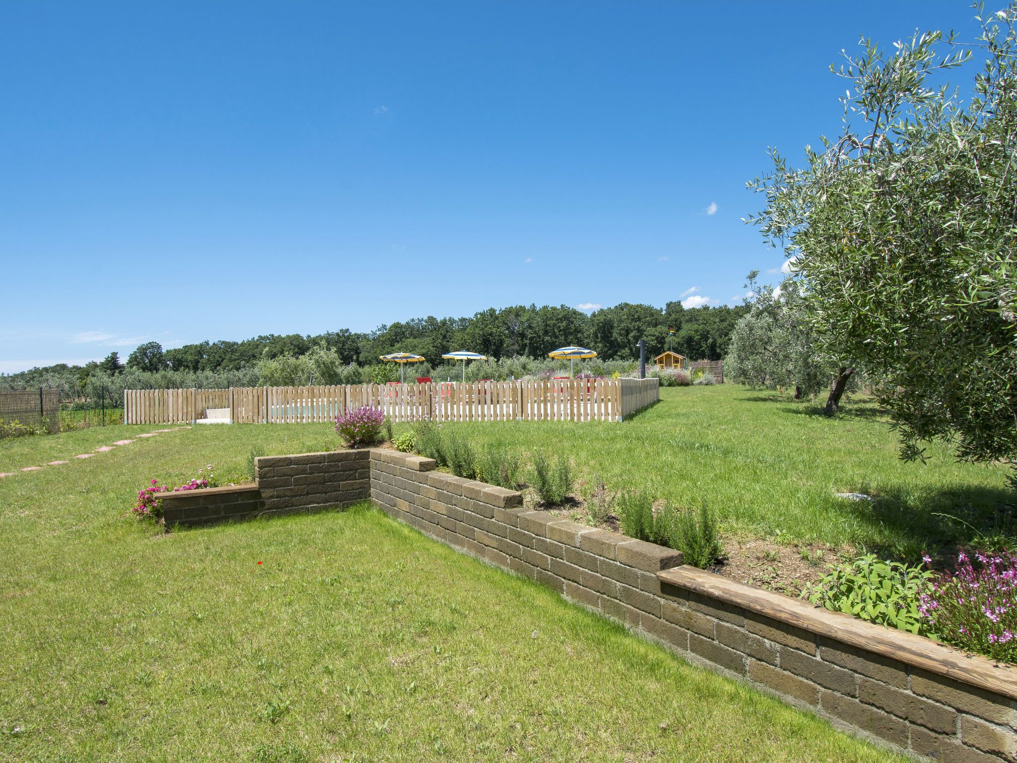 Un cortile recintato con un muro di sostegno in mattoni, un pontile in legno e diverse piante e fiori.