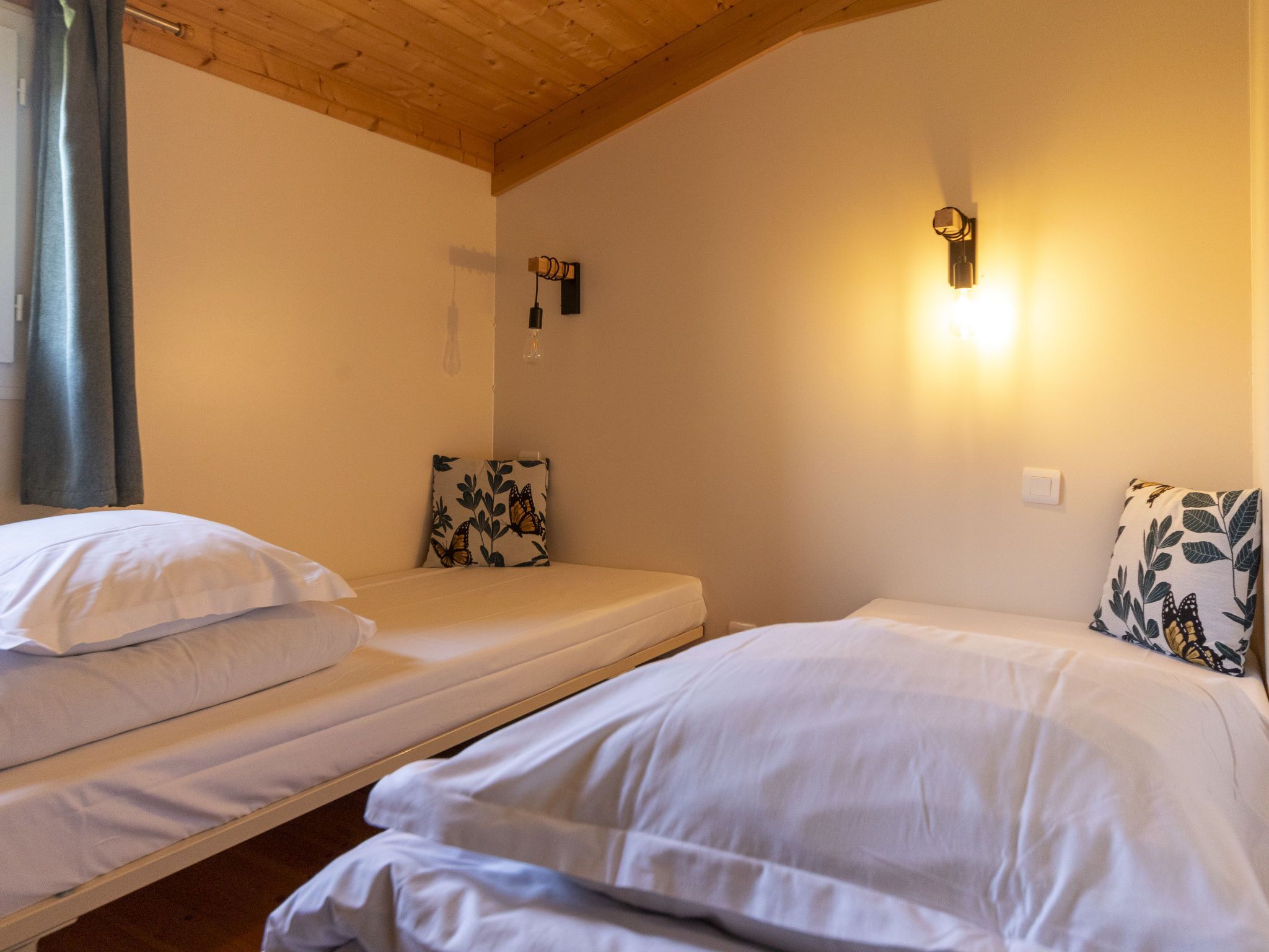 Une chambre avec deux lits simples, un plafond en bois et un luminaire fixé au mur.