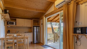 A compact kitchen with wooden cabinets, a stainless steel refrigerator, a microwave, and a dining area with a table and chairs. - Domaine de Sévenier Chêne Blanc by Interhome (Vallon-Pont-d'Arc)