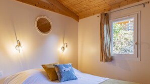A bedroom with a wooden ceiling, a round mirror, two wall-mounted lights, a window with curtains, and a bed with white bedding and two pillows. - Domaine de Sévenier Chêne Blanc by Interhome (Vallon-Pont-d'Arc)