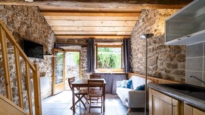 Eine gemütliche Küche mit Steinwänden, Holzbalken, einem Essbereich mit Tisch und Stühlen, einer Couch und einem an der Wand befestigten Fernseher.