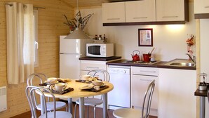 Cocina compacta con armarios blancos, microondas y lavamanos. Hay una mesa de comedor con sillas y un florero con flores sobre la encimera.