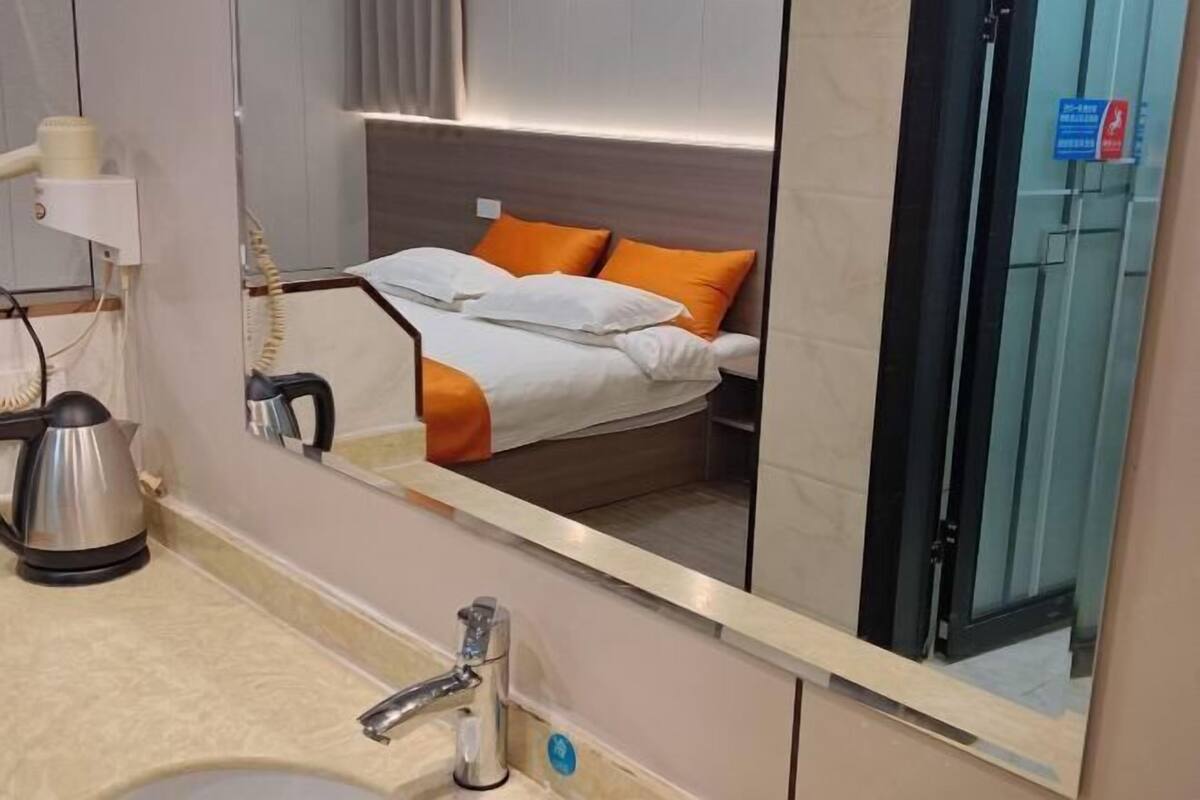 A hotel room with a bed, a mirror, a sink, and a kettle.
