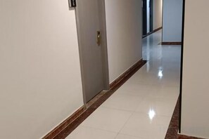 A corridor with a door on the left, a reflective tiled floor, and a plain wall. - Lake Holiday Hotel (Chizhou)