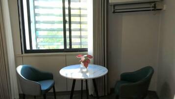 A room with two chairs, a small table with a vase, and a window with blinds.