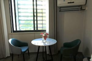 Una habitación con dos sillas, una mesita con un florero y una ventana con persianas.